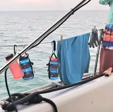 Water bottles clipped to a boat’s lifeline with carabiners, beside a towel held on with wooden clothespins